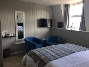 sypialnia z 2 niebieskimi krzesłami, łóżkiem i telewizorem w obiekcie Woodlands Guest House w mieście Saundersfoot