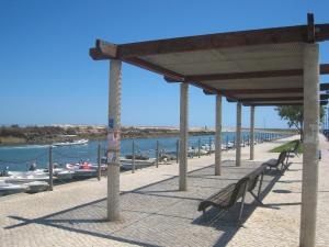 a pier with benches and boats in the water at Casa da Sardinha in Fuzeta