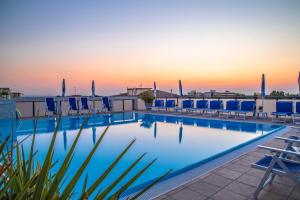 a swimming pool with chairs and a sunset in the background at Renzo Hotel in Cesenatico