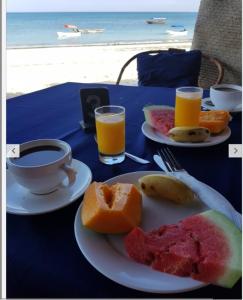 a table with two plates of fruit and a cup of coffee at Ebony & Ivory Beach Bungalows in Nungwi