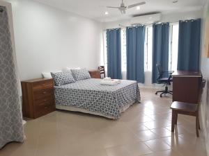 a bedroom with a bed with blue curtains and a desk at Prestige Apartments - Solomon Islands in Honiara