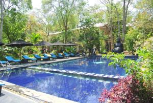 a swimming pool with blue chairs and umbrellas at Flower Garden Eco Village in Sigiriya