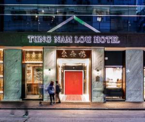 Duas pessoas à porta de uma loja com uma porta vermelha. em Tung Nam Lou Art Hotel em Hong Kong