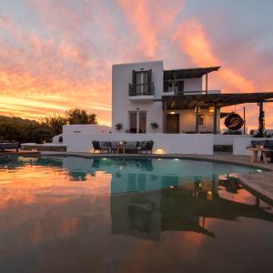 a villa with a swimming pool in front of a sunset at Olive Mykonos Villas in Ano Mera