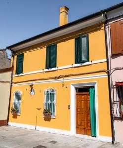 un edificio giallo con finestre con persiane verdi e una porta di La Casa di Santino a Comacchio