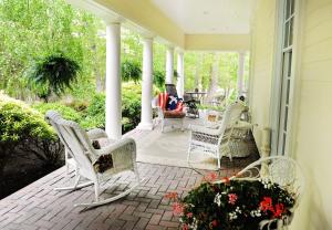un porche con sillas blancas y flores en una casa en A Walk in the Woods Bed and Breakfast en Southold