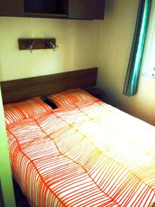 サン・ジャン・ド・モンにあるMobile homeのベッドルームにオレンジと白の掛け布団が備わるベッド1台