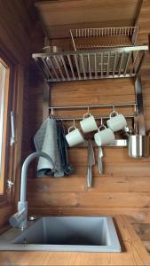 un lavandino con tazze e utensili da cucina appesi a un muro di Labrags Saulrieti a Jūrkalne