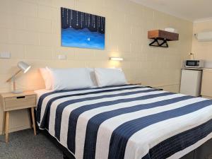 a bedroom with a bed with a blue and white striped blanket at Sail Inn Motel in Yeppoon