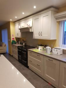 una cocina con armarios blancos y electrodomésticos negros en Causeway Coast Carrivcashel Holiday Home, en Ballymoney