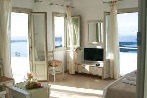 a bedroom with a bed and a tv and windows at Irida - Santorini in Imerovigli
