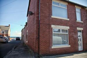 a red brick building with a window on a street at The Mules in Newbiggin-by-the-Sea