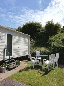 three white chairs and a table in a yard at Swanage bay caravan in Swanage
