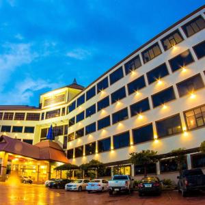 un grand bâtiment avec des voitures garées dans un parking dans l'établissement Golden Dragon Resort, à Singburi