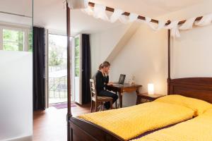 une femme assise sur un bureau avec un ordinateur portable dans une chambre dans l'établissement Kulturhotel Guggenheim, à Liestal