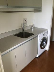 een keuken met een wastafel en een wasmachine bij Nikau’s on Palmer in Foxton Beach