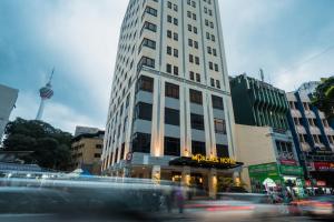 a tall white building on a city street with cars at MPalace Hotel KL in Kuala Lumpur