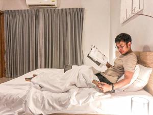 a man sitting on a bed reading a book at Lemonade Phuket Hotel -SHA Plus in Chalong