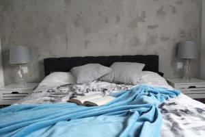 a bed with a blue blanket and a book on it at Apartament Wilanów Klimczaka in Warsaw