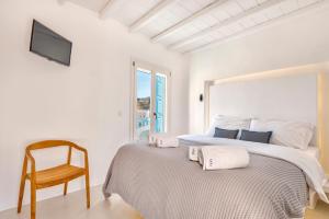 a white bedroom with a bed and a chair at Mykonian Mews Luxury Suites in Psarou