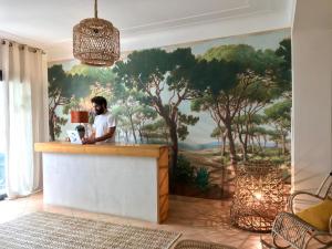 un homme debout à un comptoir avec une fresque murale d'arbres dans l'établissement Casa Orfea, à Algajola