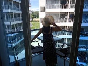 a woman in a straw hat looking out a window at a balcony at Grand Blue Condominium by Mary in Mae Pim