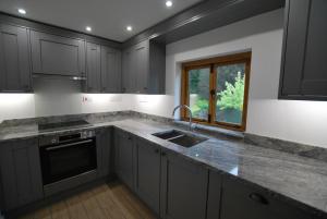 cocina con armarios grises, fregadero y ventana en The Coach House Annexe, en Llangollen