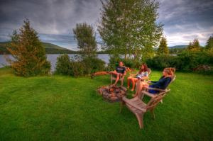 three people sitting on a fire pit in the grass at Le Chalet Relax du Lac St-Tite in Saint-Tite-des-Caps