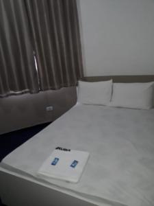 Una cama blanca con mando a distancia. en Hotel Aruba, en Curitiba