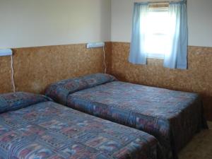 two beds in a hotel room with a window at Hôtel Motel du Rocher in Rivière-la-Madeleine