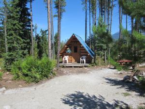 a small cabin in the woods with two white chairs at Blue River Campgrounds & Cabin-public washroom in Blue River +41 photos