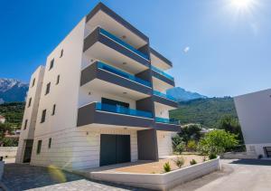 a white building with blue balconies and mountains in the background at Villa Ivo Apartmani in Promajna