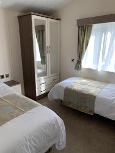 a bedroom with two beds and a dresser and a mirror at Riverside Rothbury Superior Lodge in Rothbury