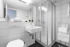 a white bathroom with a sink and a mirror at Seehotel Baumgarten in Kehrsiten