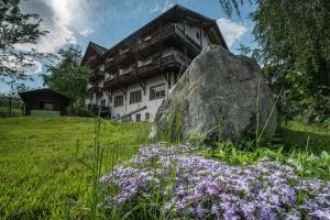 Hotel Ucliva في Waltensburg: منزل به صخرة كبيرة وورود أرجوانية
