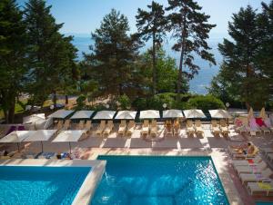 a swimming pool with chairs and umbrellas and the ocean at Hotel Excelsior - Liburnia in Lovran