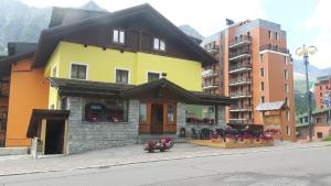 une maison jaune avec des fleurs sur le côté d'une rue dans l'établissement Hotel Angelo, à Passo del Tonale