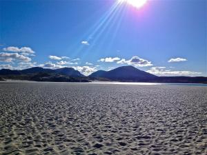 a sandy beach with the sun in the sky at Otter Bunkhouse in Cairisiadar