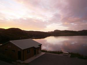 a cabin on the side of a lake at sunset at Otter Bunkhouse in Cairisiadar