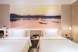 twee bedden in een hotelkamer met een schilderij van een meer bij Atour Hotel (Kong Family Mansion) in Qufu