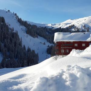 ein rotes Gebäude auf einem schneebedeckten Hang mit einem Berg in der Unterkunft Ländle Hotel in Damüls