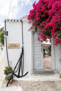 a white building with pink flowers and a door at Hotel Miranda in Hydra