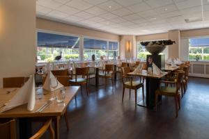 um restaurante com mesas e cadeiras de madeira e janelas em Fletcher Resort-Hotel Zutphen em Zutphen