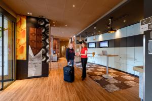 a man and a woman with a suitcase in a lobby at ibis Winterthur City in Winterthur