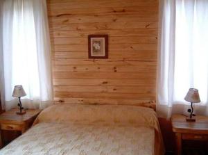 1 dormitorio con 1 cama con paredes de madera y 2 ventanas en Cabañas En el Corazón del Bosque en San Carlos de Bariloche