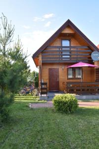 Cabaña de madera con porche y sombrilla rosa en Domki na Różanej 2 en Rowy
