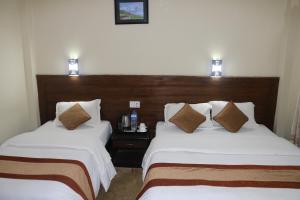 2 camas en una habitación de hotel con sábanas blancas y almohadas marrones en Chitwan Village Resort, en Sauraha