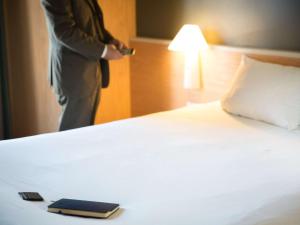 Un uomo in giacca e cravatta è in piedi accanto a un letto di Hotel Ibis Firenze Nord Aeroporto a Sesto Fiorentino