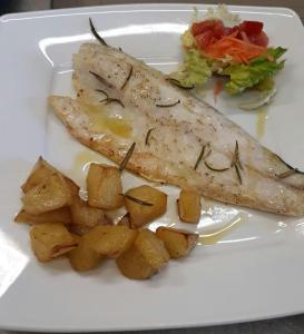 a white plate with a piece of fish and potatoes at Hotel ILLI in Marina di Massa