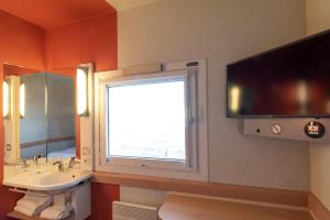 a bathroom with a sink and a window and a television at ibis budget Viry-Chatillon A6 in Viry-Châtillon